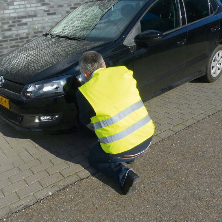 Mand iført refleksvest voksen – gul sikkerhedsvest knæler foran sort bil.